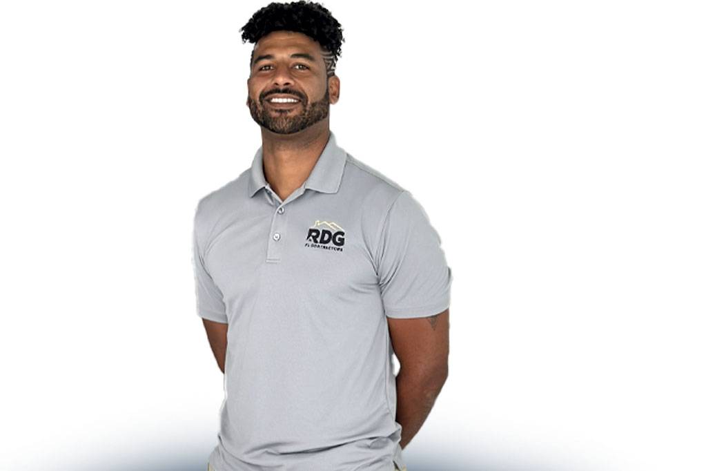 Dan-Ready-2-Help- A person wearing a light gray polo shirt with an RDG logo stands confidently.
